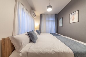 A neatly made bed with white and gray bedding, a wooden headboard, and a bedside table. - Eldor NishiKojiya Apartment (Tokyo)
