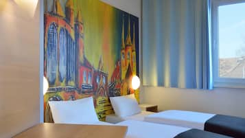 Ein Hotelzimmer mit zwei Betten, einem Gemälde einer Kirche an der Wand, einem Fenster mit Vorhängen und einem Nachttisch mit Lampe.