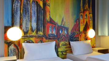 A hotel room with two beds, a colorful mural of a building, and two bedside lamps.