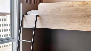 Una cama litera con cabecera de madera, una escalera metálica y una ventana con vistas a edificios.