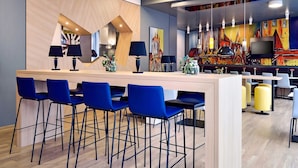 Un espace bar moderne avec un comptoir en bois, des tabourets de bar bleus et une fresque murale colorée.