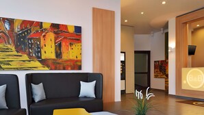 Un hall d’entrée moderne avec un canapé noir, une table jaune et un tableau abstrait aux couleurs vives accroché au mur.