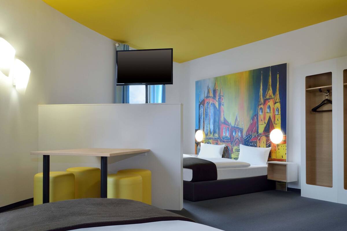 Une chambre d’hôtel moderne, équipée d’un lit, d’un bureau et d’un tableau représentant une cathédrale.
