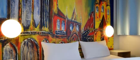 Una habitación de hotel con una cama grande, dos mesitas de noche y un mural colorido de un edificio en la pared.