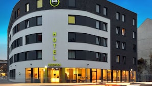 Un hôtel moderne à la façade incurvée, doté d’un espace d’accueil et d’une enseigne bien visible indiquant qu’il fait partie de la chaîne B&B Hotels.