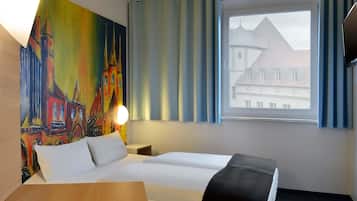 Ein Hotelzimmer mit Bett, Schreibtisch, einem Bild eines Gebäudes und einem Fenster mit Vorhängen.