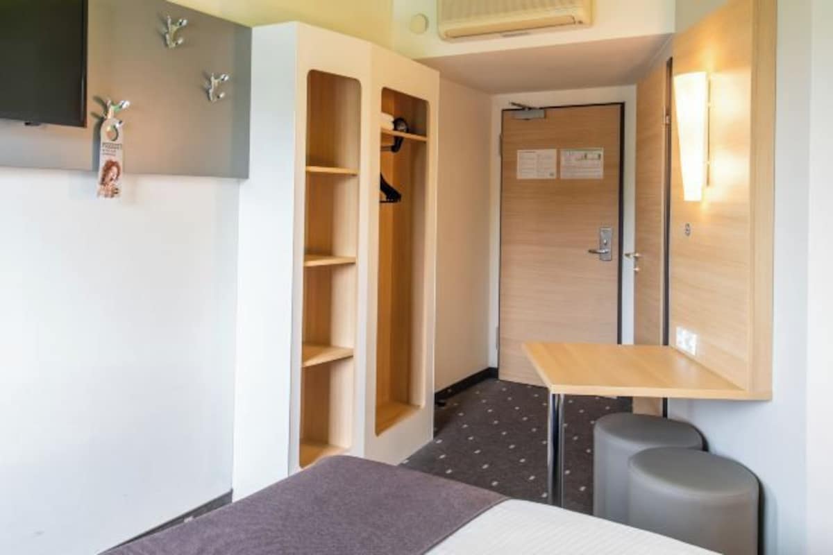 Una habitación de hotel con una cama, un escritorio, un armario y un pequeño rincón de descanso.