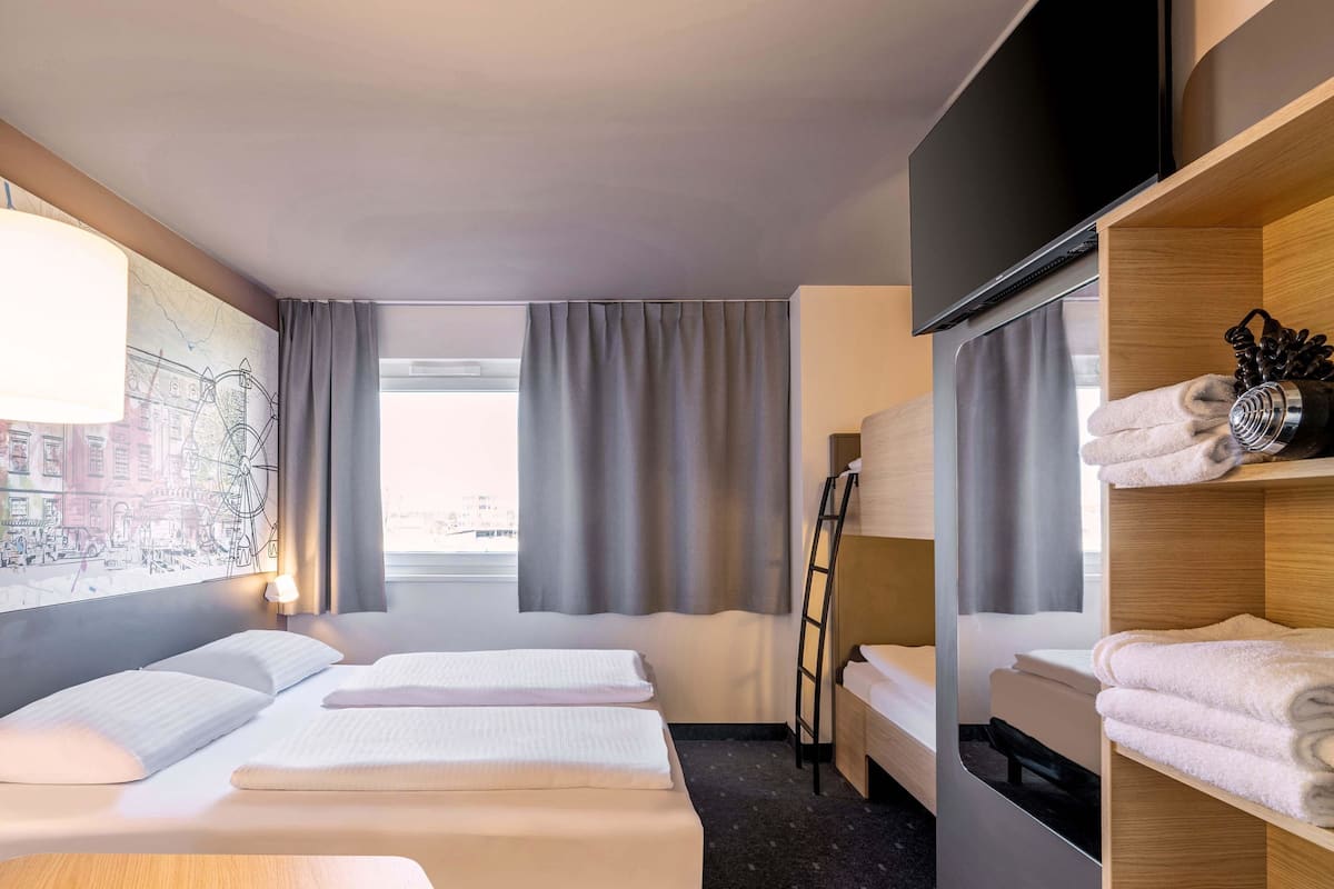A hotel room with two beds, a TV, a map artwork, a window with curtains, and a shelf with towels.