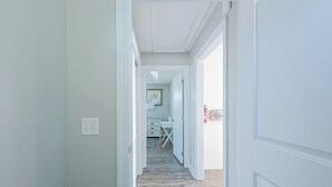 A hallway with a wooden floor leading to a room with a desk and chair.