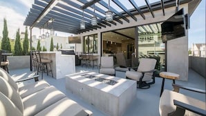 A rooftop terrace with outdoor seating, a fire pit, and a pergola with hanging lanterns.