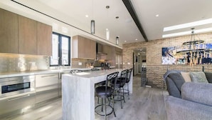 A modern kitchen with a marble island, bar stools, and a large window.