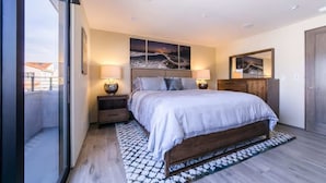 A modern bedroom with a large bed, bedside lamps, a wooden headboard, and artwork on the walls.