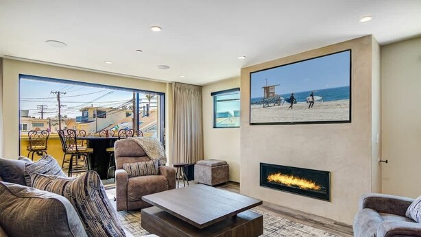 A spacious living room with a large window, a fireplace, and a beach-themed artwork.