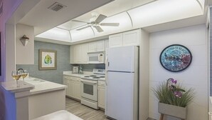 A modern kitchen with white cabinetry, a microwave, stove, and refrigerator. There is a ceiling fan, a framed artwork on the wall, and a potted plant. - Oceanfront Beach House w/ Family Amenities (Satellite Beach)