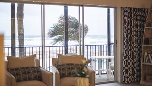 A room with a large sliding glass door leading to a balcony with a view of the beach and palm trees. - Oceanfront Beach House w/ Family Amenities (Satellite Beach)