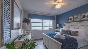 A bedroom with a bed, a ceiling fan, a window with a view, a desk with a lamp, and a plant. - Oceanfront Beach House w/ Family Amenities (Satellite Beach)