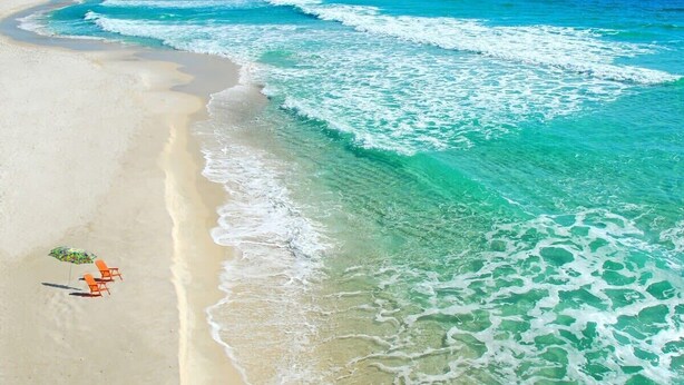 A beach with clear turquoise water, a sandy shore, and a sailboat in the distance. - Oceanfront Beach House w/ Family Amenities (Satellite Beach)