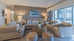 A living room with a large window, a wooden wall, and a sofa set. - Oceanfront Beach House w/ Family Amenities (Satellite Beach)
