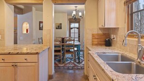 A kitchen with granite countertops, wooden cabinets, a stainless steel sink, and a window with blinds. - Comfortable Family Home, Walk to The Plaza (Santa Fe)