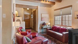 A cozy living room with leather sofas, a patterned rug, and a large window with blinds. - Comfortable Family Home, Walk to The Plaza (Santa Fe)