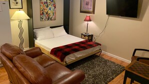 A bedroom with a bed, a brown leather sofa, a small table, a lamp, and two framed pictures on the wall. - Lovelock Pet-Friendly Studio Next to I-80 (Lovelock)
