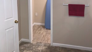 A hallway with a white door, a blue ironing board, a red towel on a rack, and a framed picture on the wall. - Lovelock Pet-Friendly Studio Next to I-80 (Lovelock)
