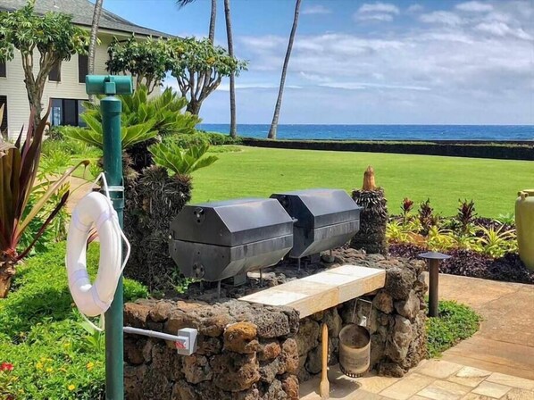 An outdoor grill setup with a stone wall, a hose, and a view of the ocean.