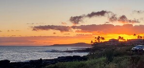 Um pôr do sol costeiro com vista para o oceano e colinas distantes.