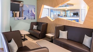 Un espacio lounge moderno con sofás de cuero y mesas, un televisor grande montado en la pared y obras de arte con paisajes urbanos.