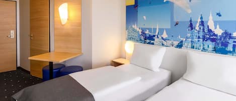 A hotel room with two beds, a wooden desk, a wall-mounted light, and a cityscape mural.