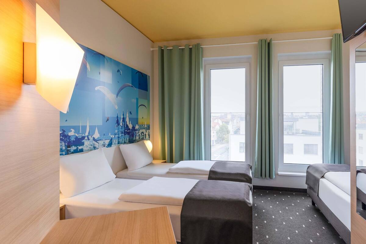 A hotel room with a bed, a sofa, a desk, and a large window with curtains.