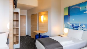 Habitación de hotel con cama, escritorio, silla, armario y una pared con un mural de paisaje urbano.