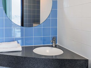 A bathroom with a round mirror, a white sink, and blue tiled walls. - B&B HOTEL Fulda-City (Fulda)