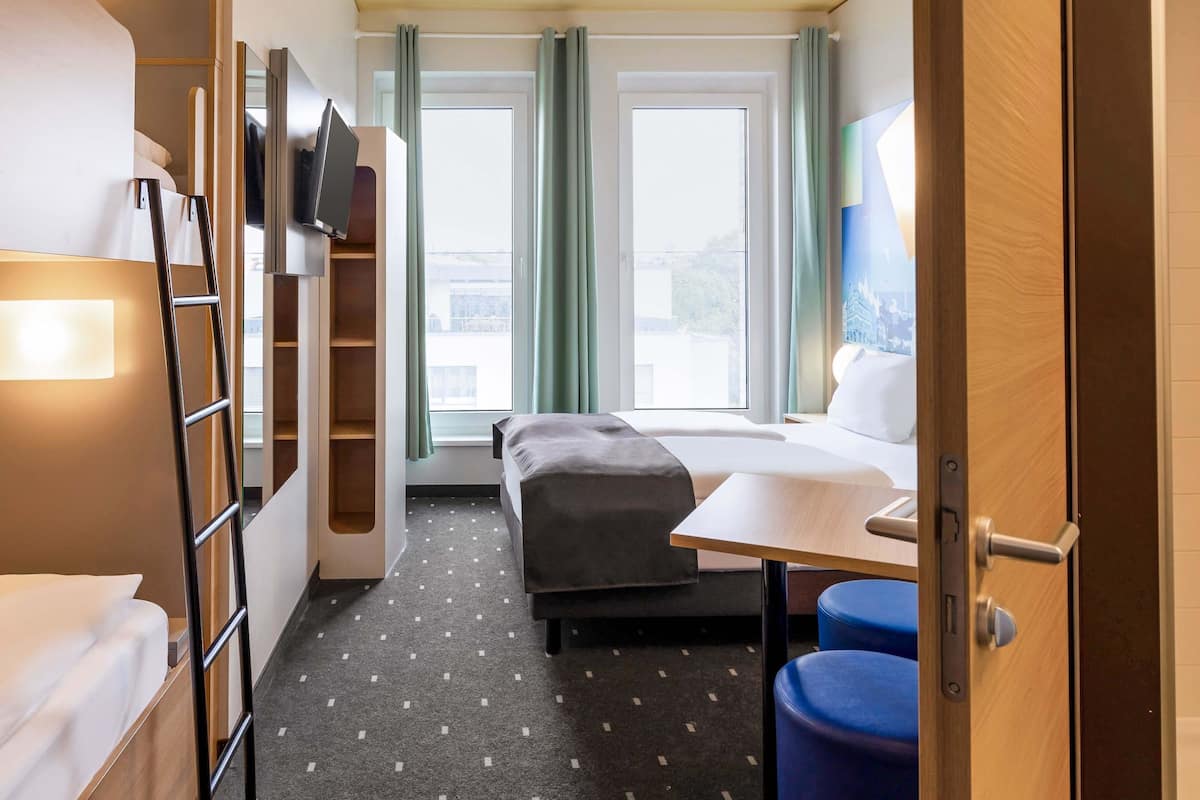 A compact hotel room with a bunk bed, a desk, and a small seating area.