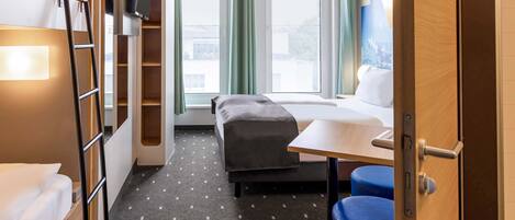 A compact hotel room with a bunk bed, a desk, and a small seating area.