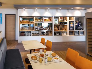 A modern dining area with a buffet setup, including various food items and a coffee machine. - B&B HOTEL Fulda-City (Fulda)