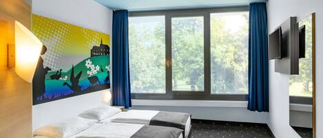 A hotel room with two beds, a desk, a chair, a TV, and a large window with curtains.