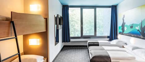 Une chambre d’hôtel avec un lit superposé, deux lits simples, un bureau et une grande fenêtre avec des rideaux.