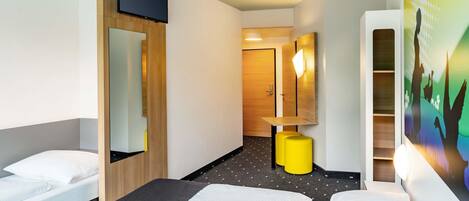 A hotel room with a bed, a desk, a mirror, and a wall-mounted TV.