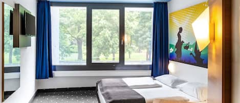 A hotel room with a bed, a small table, a chair, a TV, and a window with curtains.