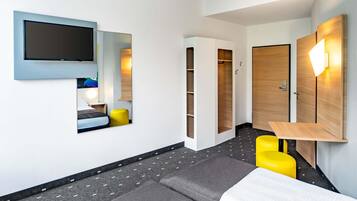 Una habitación de hotel moderna con una cama, un televisor montado en la pared, un armario y una pequeña mesa.