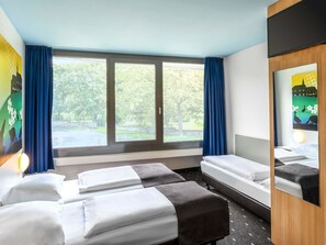 Une chambre d’hôtel avec deux lits, une grande fenêtre avec des rideaux, un miroir et une vue sur la verdure.