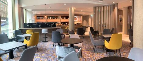 A modern hotel lobby with a bar area, seating arrangements, and large windows offering a view of the street.