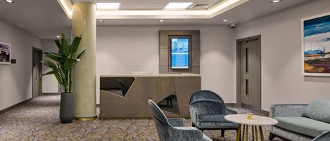 A modern hotel lobby with a reception desk, seating area, and a large plant.