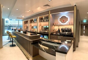 Zona de bar moderna con mostrador, taburetes y estantes llenos de botellas.