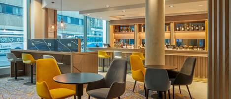 A modern bar area with seating and a bar counter, featuring a patterned carpet and large windows.