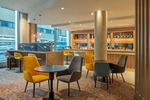A modern bar area with seating and a bar counter, featuring a patterned carpet and large windows.