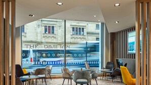 A modern hotel lobby with a large window view of a street, featuring a blue bus with floral patterns. - Maldron Hotel Glasgow City (Glasgow)