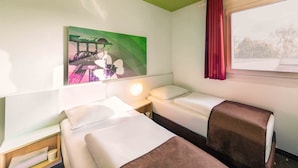 Une chambre d’hôtel avec deux lits, une table de chevet, une lampe, un tableau et une fenêtre avec des rideaux.