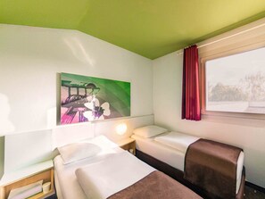Ein Hotelzimmer mit zwei Betten, einem Nachttisch, einer Lampe, einem Bild und einem Fenster mit Vorhängen.